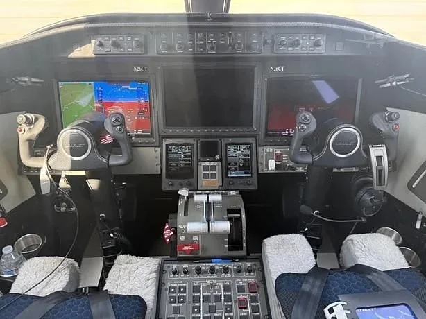 The cockpit of a business jet, showing the instrument panel with multiple large digital displays, yokes, and throttle quadrant, with N26CT visible.