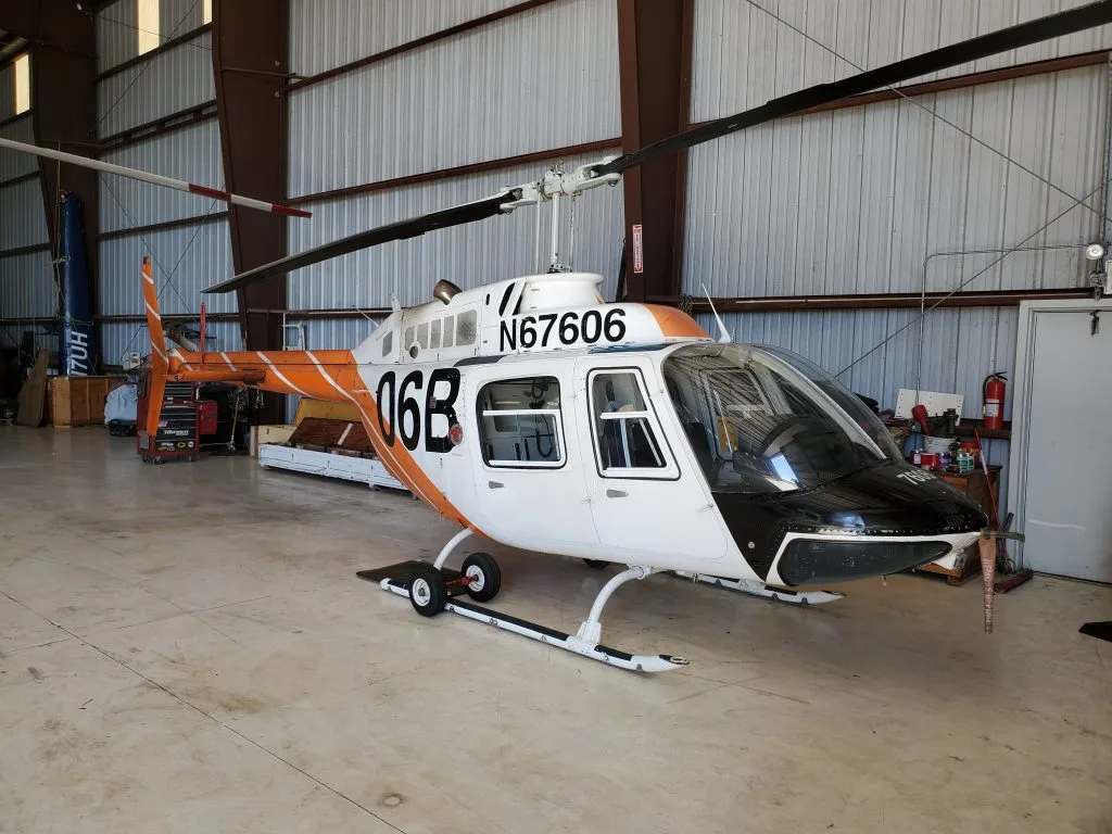 A white helicopter with orange and black accents, registration N67606, is parked inside a hangar.