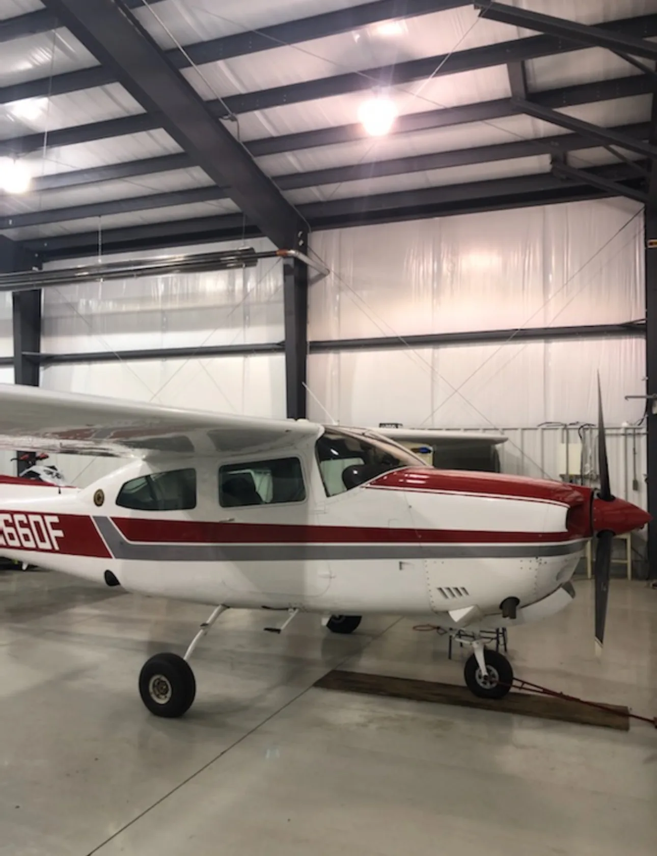 Side view of a white and red Cessna Centurion aircraft N66DF in a hangar.