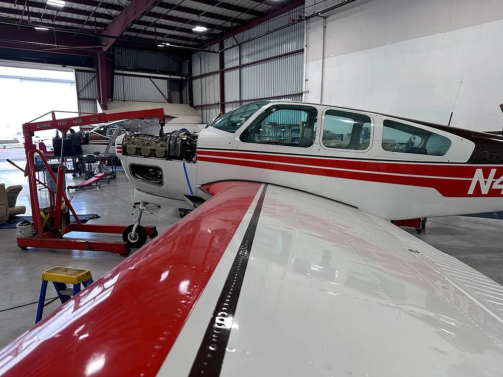 A white and red aircraft with its engine cowling open, undergoing maintenance in a hangar.