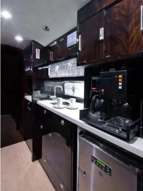 The galley of a private jet, featuring dark wood cabinetry, a sink, coffee maker, and refrigerator.
