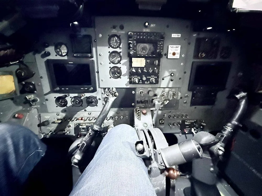 The cockpit of a BAC Strikemaster Mk.88 showing the instrument panel, controls, and a pilot's legs.
