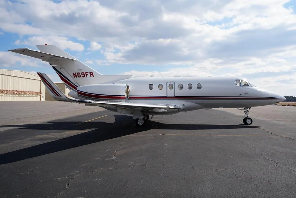 A side view of the white business jet N69FR from the rear-right, showing its tail, engine, and red and blue stripes.