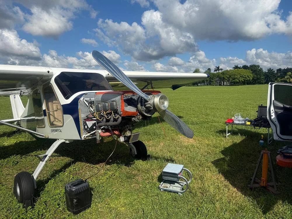 The experimental aircraft N220EX with its engine cowling removed, revealing the engine, parked on a grassy field.