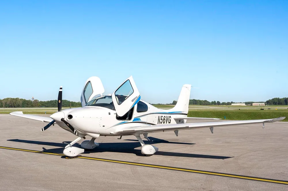 A white Cirrus SR22 aircraft with blue and black stripes, tail number N56VG, parked on an airfield with its gull-wing doors open.