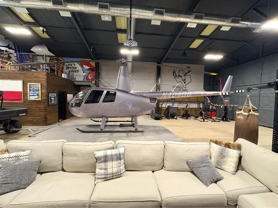 A grey Robinson R44 helicopter displayed in a large, decorated room with a couch in the foreground.