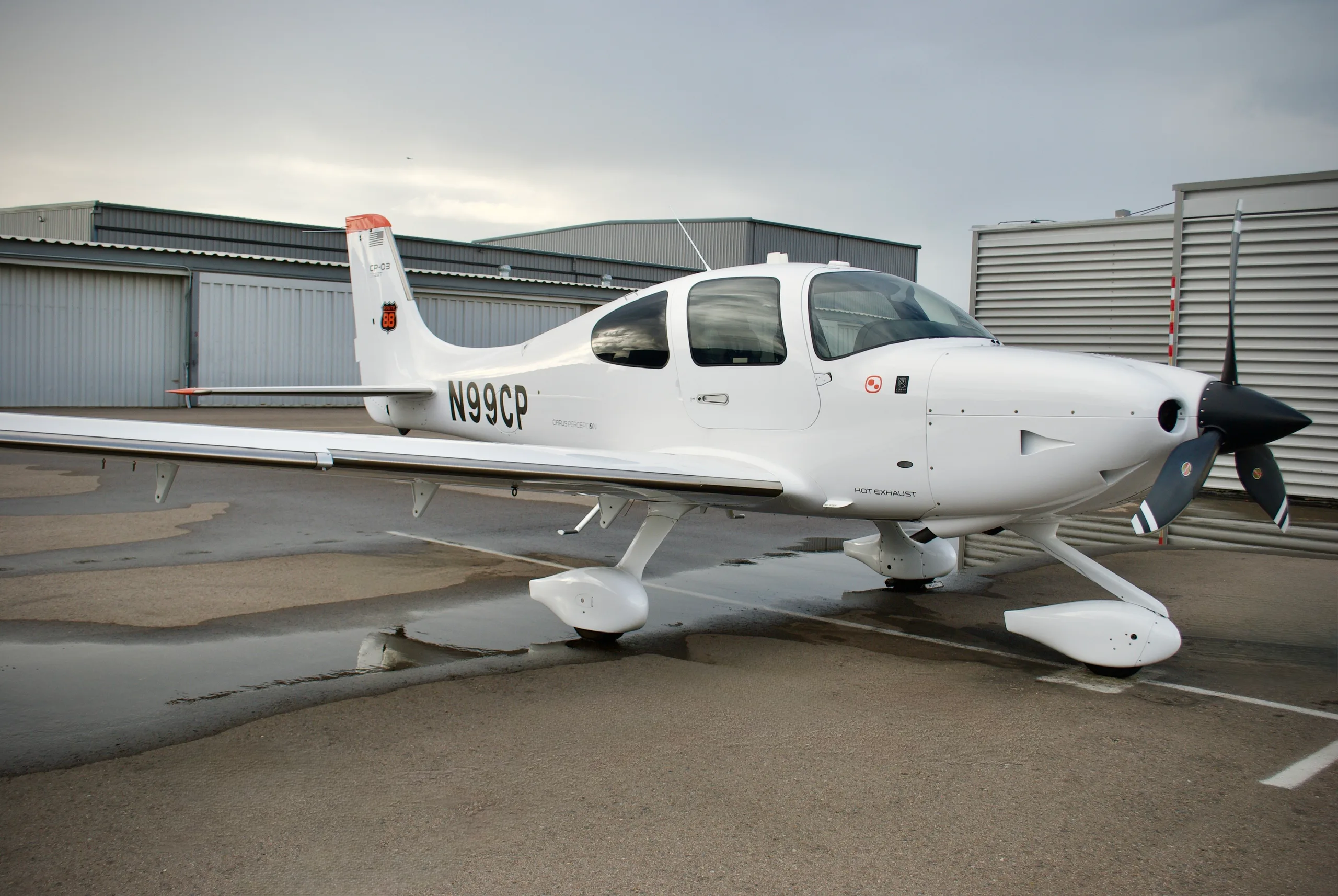 A white Cirrus SR22T aircraft with registration N99CP parked on a wet tarmac, viewed from the front-right.
