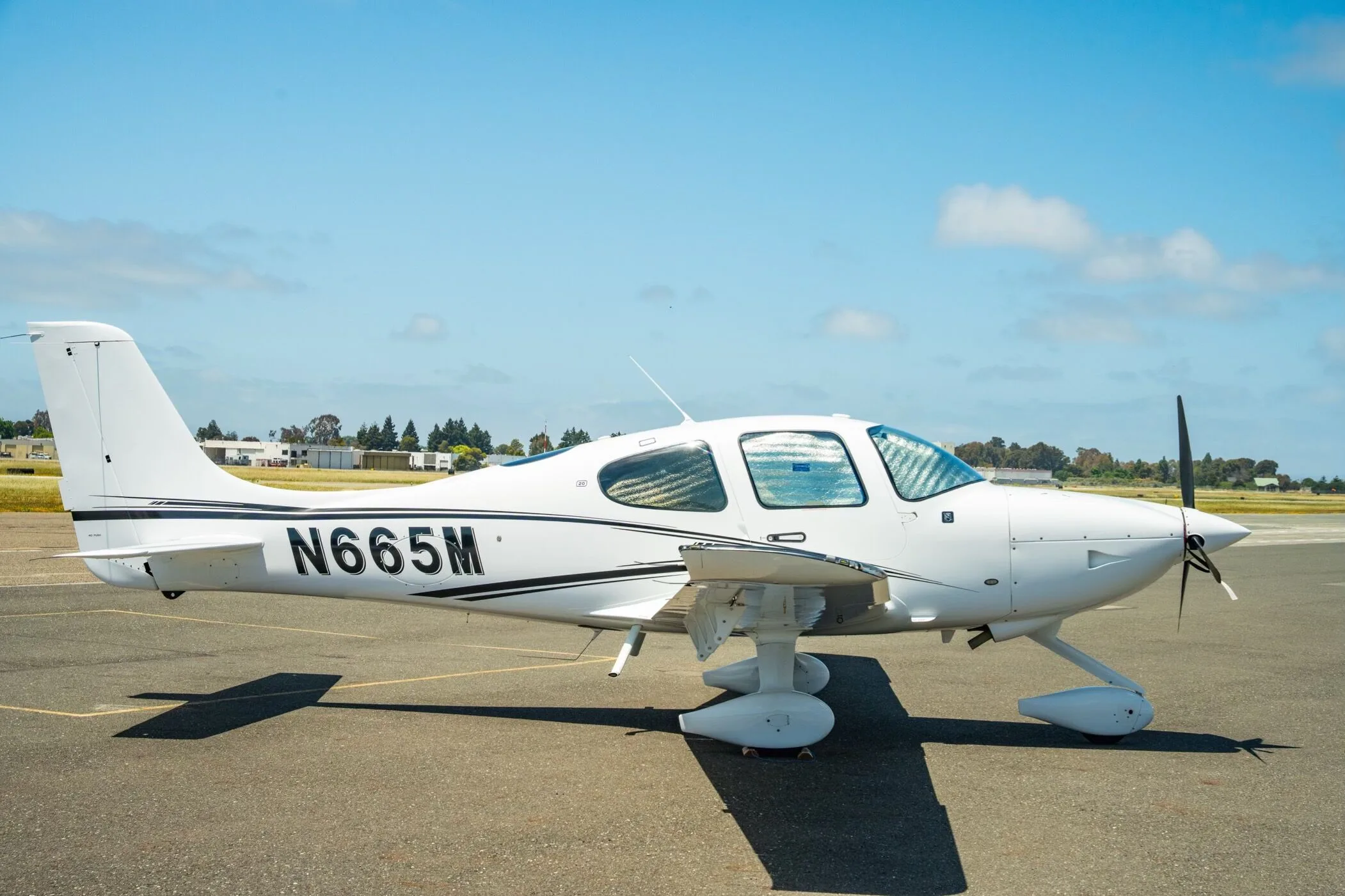 A white Cirrus SR22 aircraft with registration N665M parked on the tarmac with sun shades in the windows.