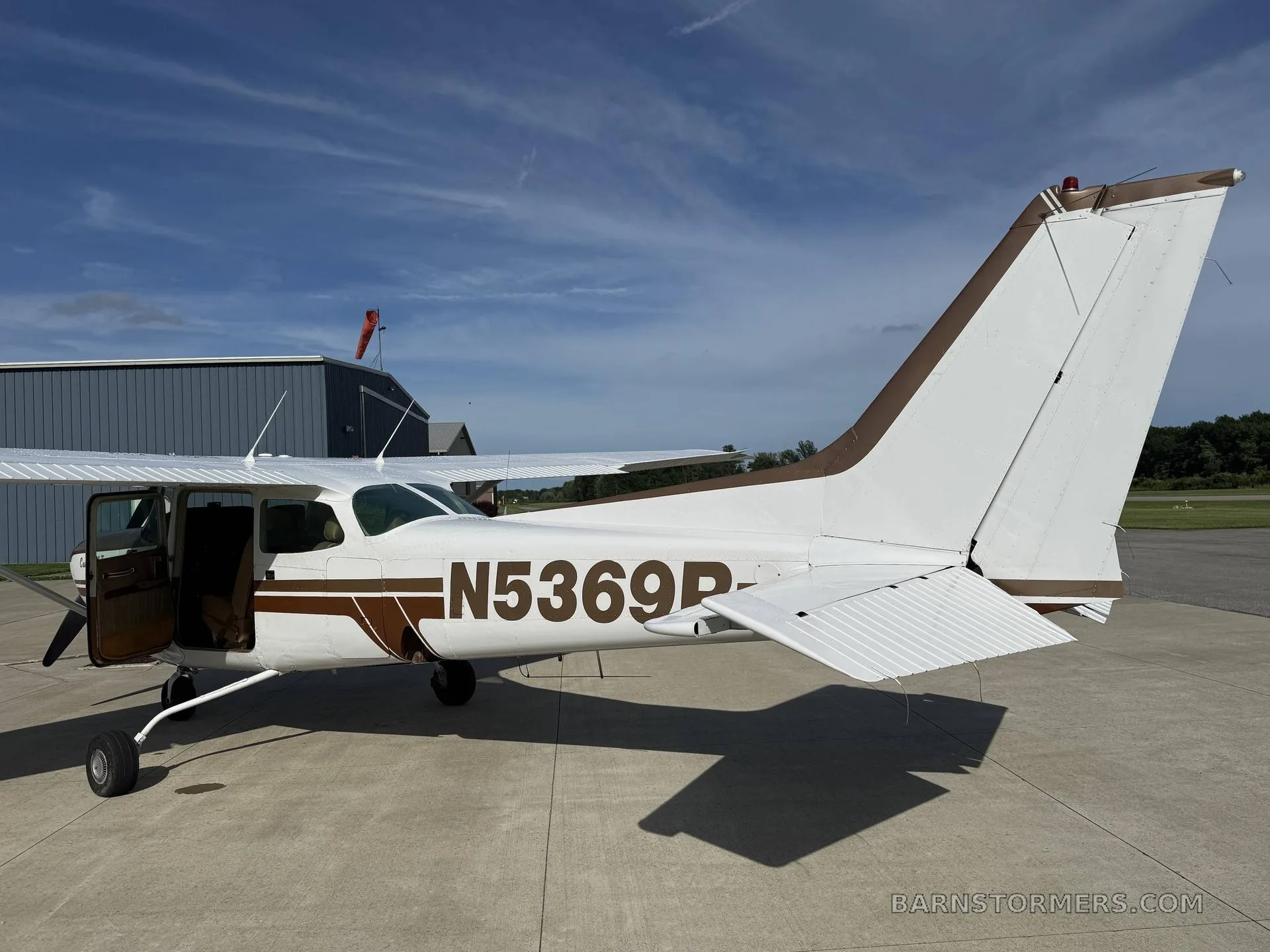 A rear-side view of a white and brown Cessna Cutlass RG II (N5369R) parked on an airfield with its door open.