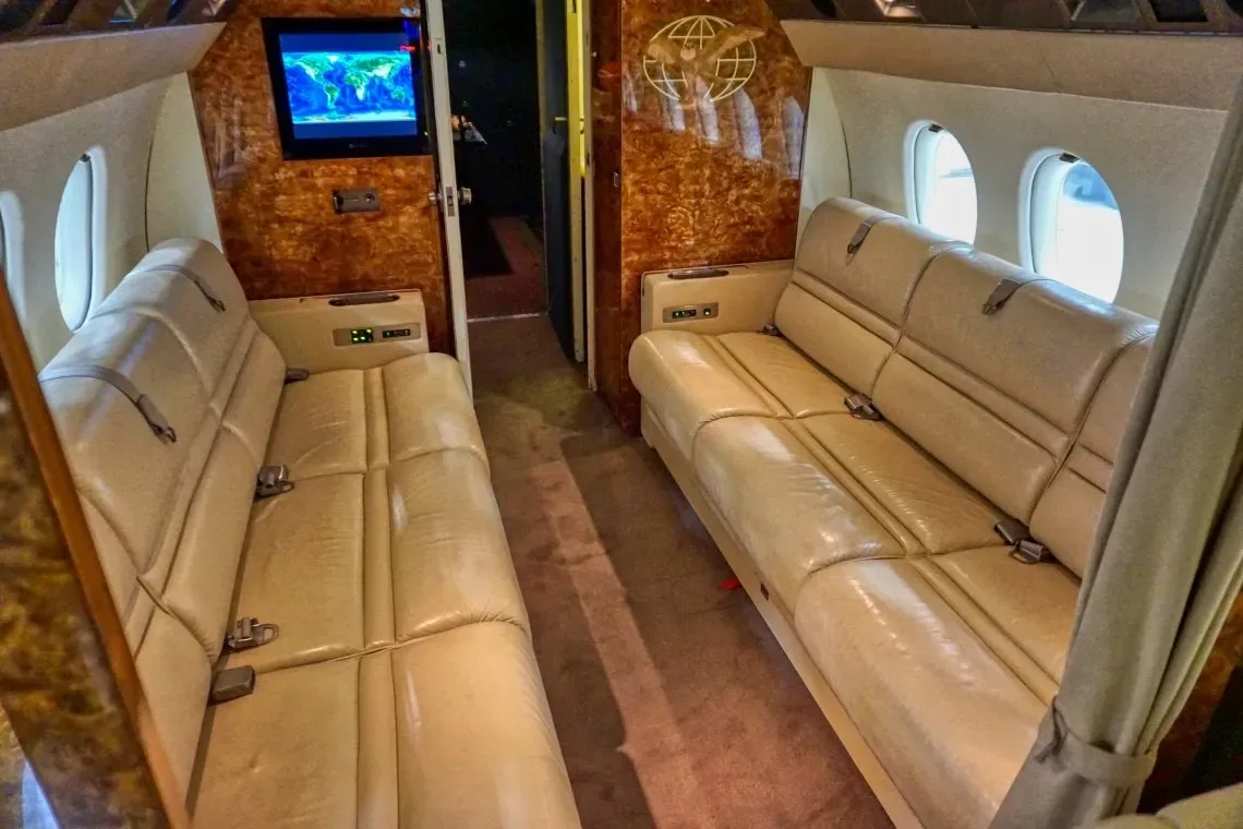 Interior view of the aircraft cabin with leather bench seats and a television.