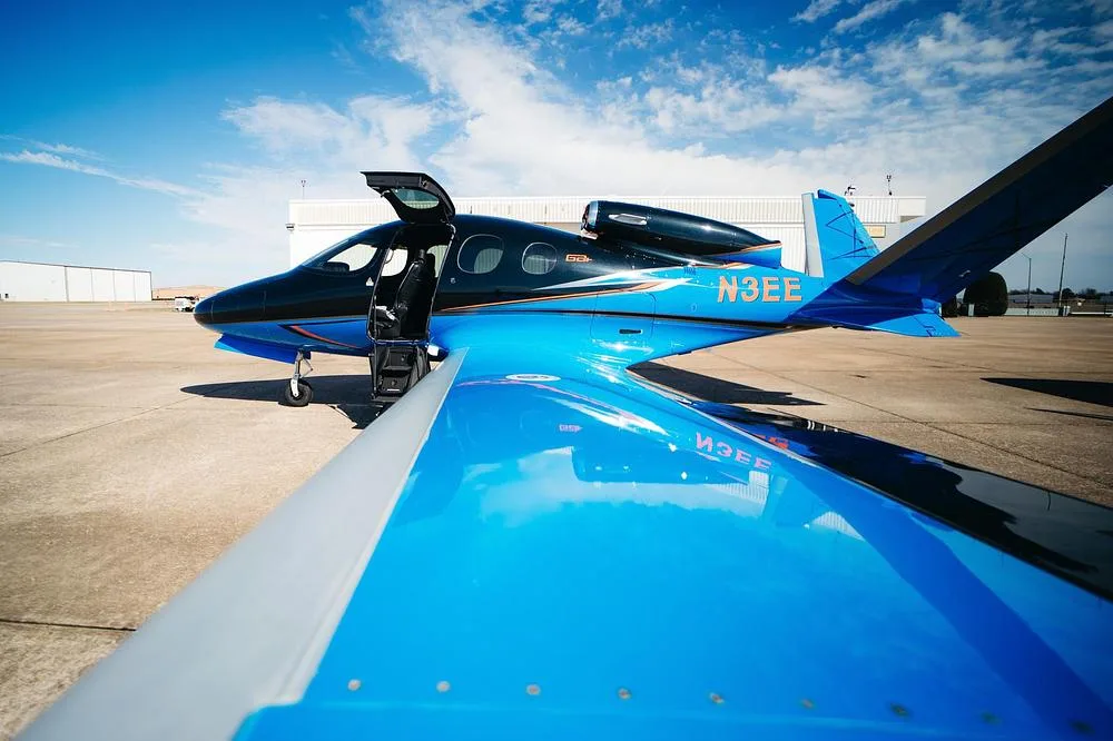 A wide-angle view of the blue and black Cirrus Vision Jet (N3EE) with its entry door open on an airfield.