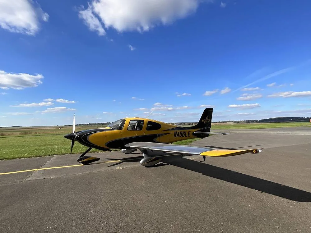 A yellow and black Cirrus SR22 aircraft with registration N456LE parked on an airfield under a blue sky.