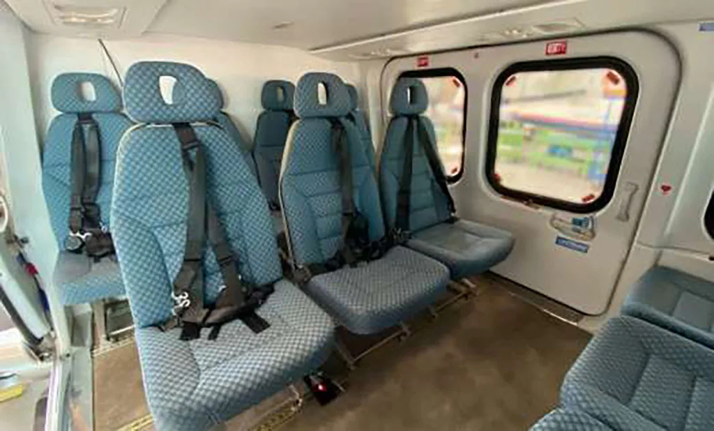 The interior cabin of a helicopter showing multiple rows of blue patterned passenger seats.