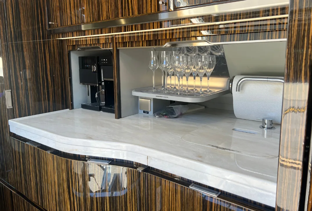 Aircraft galley with a coffee machine, glassware, and marble countertop.