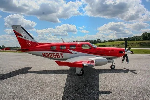 A red and white Piper M600 SLS aircraft with registration N325ST is parked on an asphalt ramp under a partly cloudy sky, viewed from the left side.