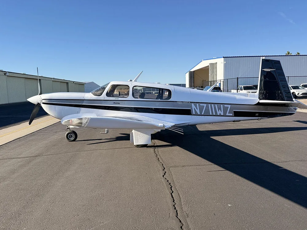A white Mooney aircraft with black and grey stripes, tail number N711WZ, parked on an airfield.