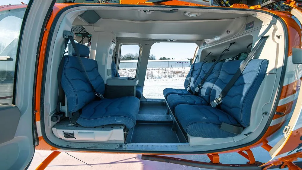The interior cabin of a helicopter showing two rows of blue fabric seats with seatbelts.