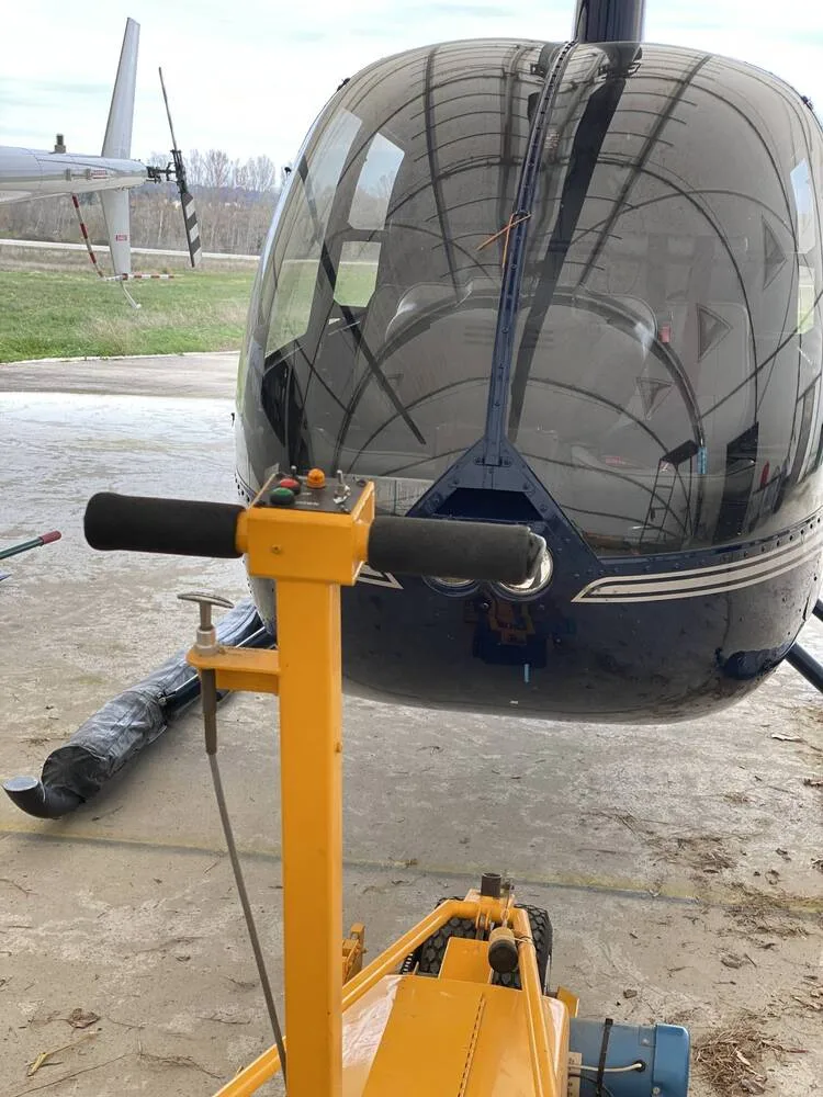 A close-up view of the front of a dark blue Robinson R44 Clipper II helicopter, N144LR, with a yellow ground handling cart in the foreground.
