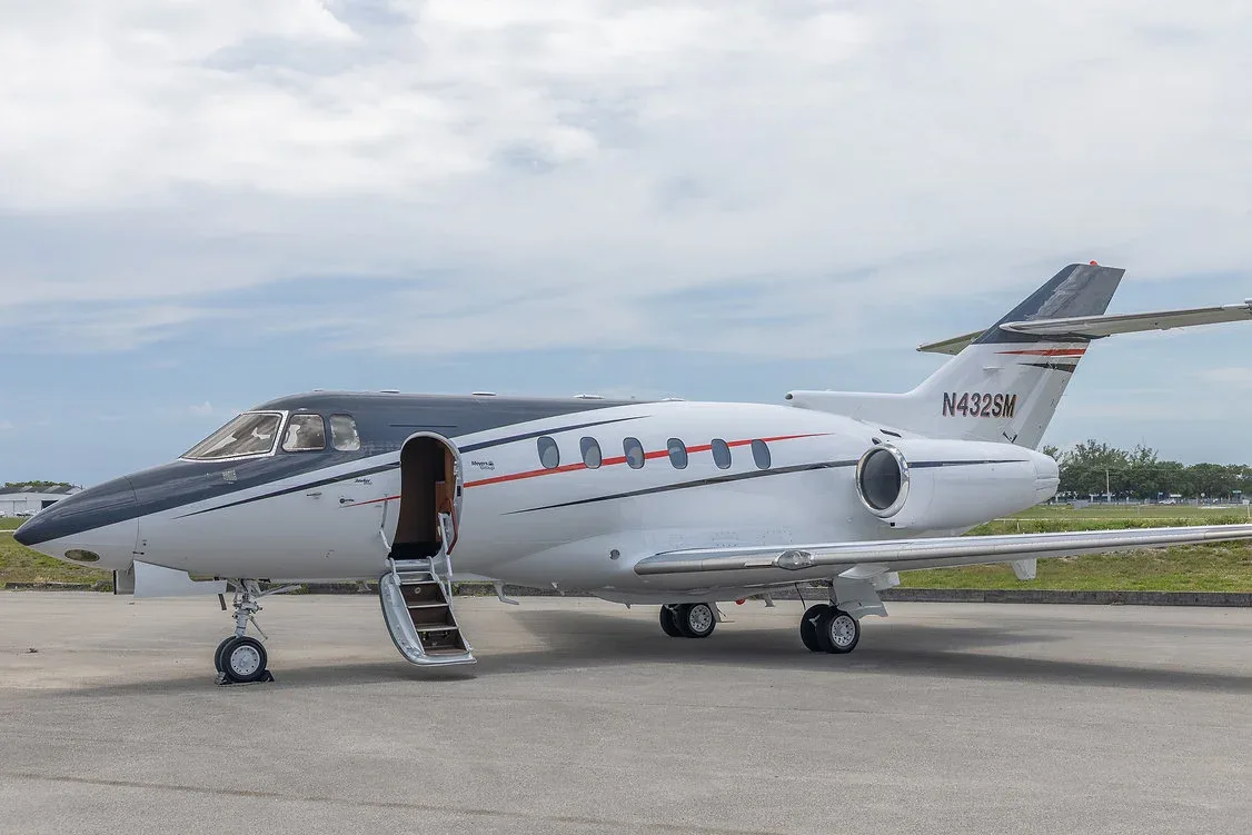 A white and black business jet, registration N432SM, with its passenger door open and stairs extended, parked on an airfield.