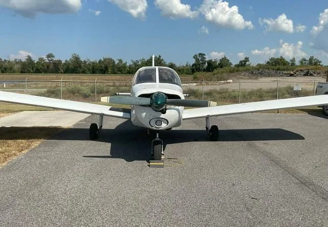 A front view of a white Piper Cherokee with green propeller tips, parked on an asphalt ramp.