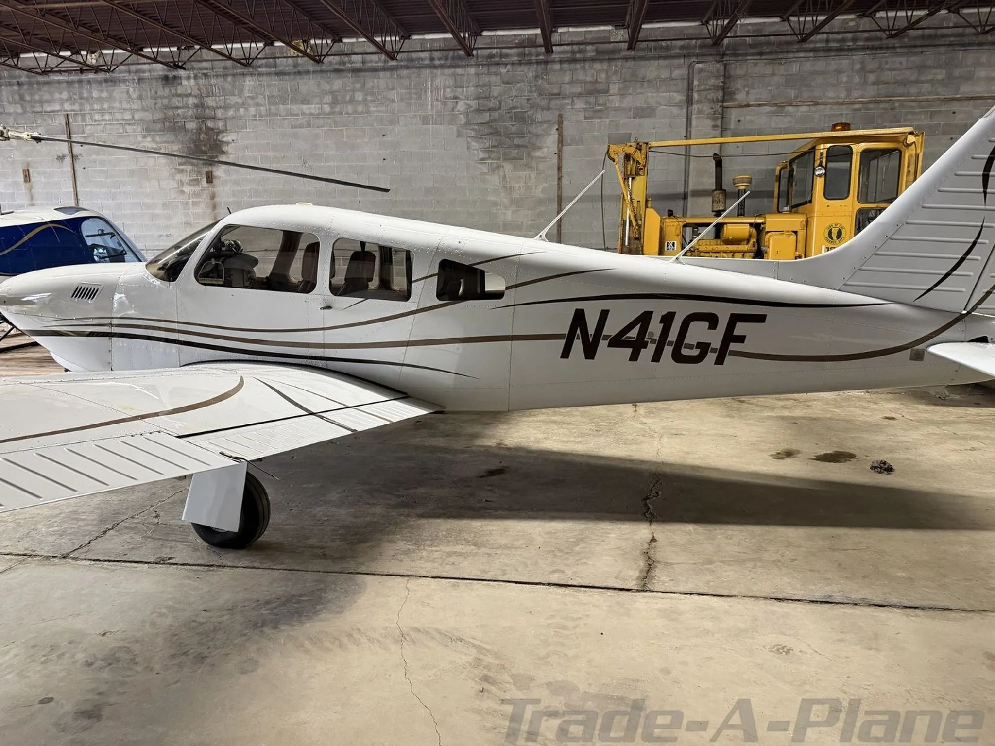 A full side view of the white Piper aircraft N41GF with brown stripes, parked in a hangar.