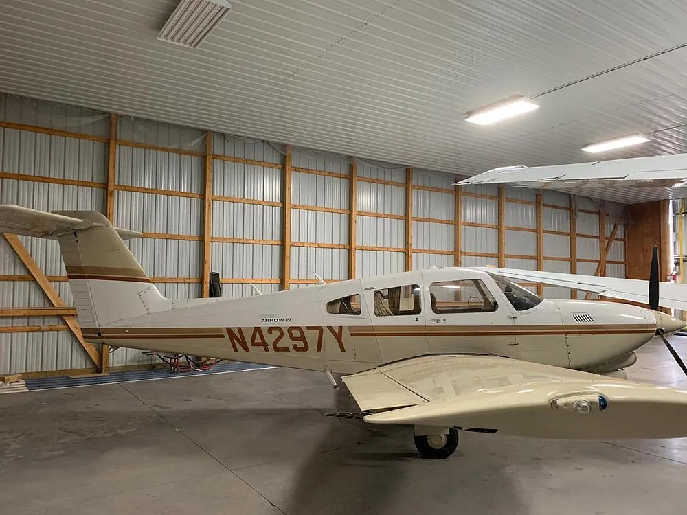 A side view of the Piper Arrow IV aircraft, N4297Y, with white and brown stripes, inside a hangar.