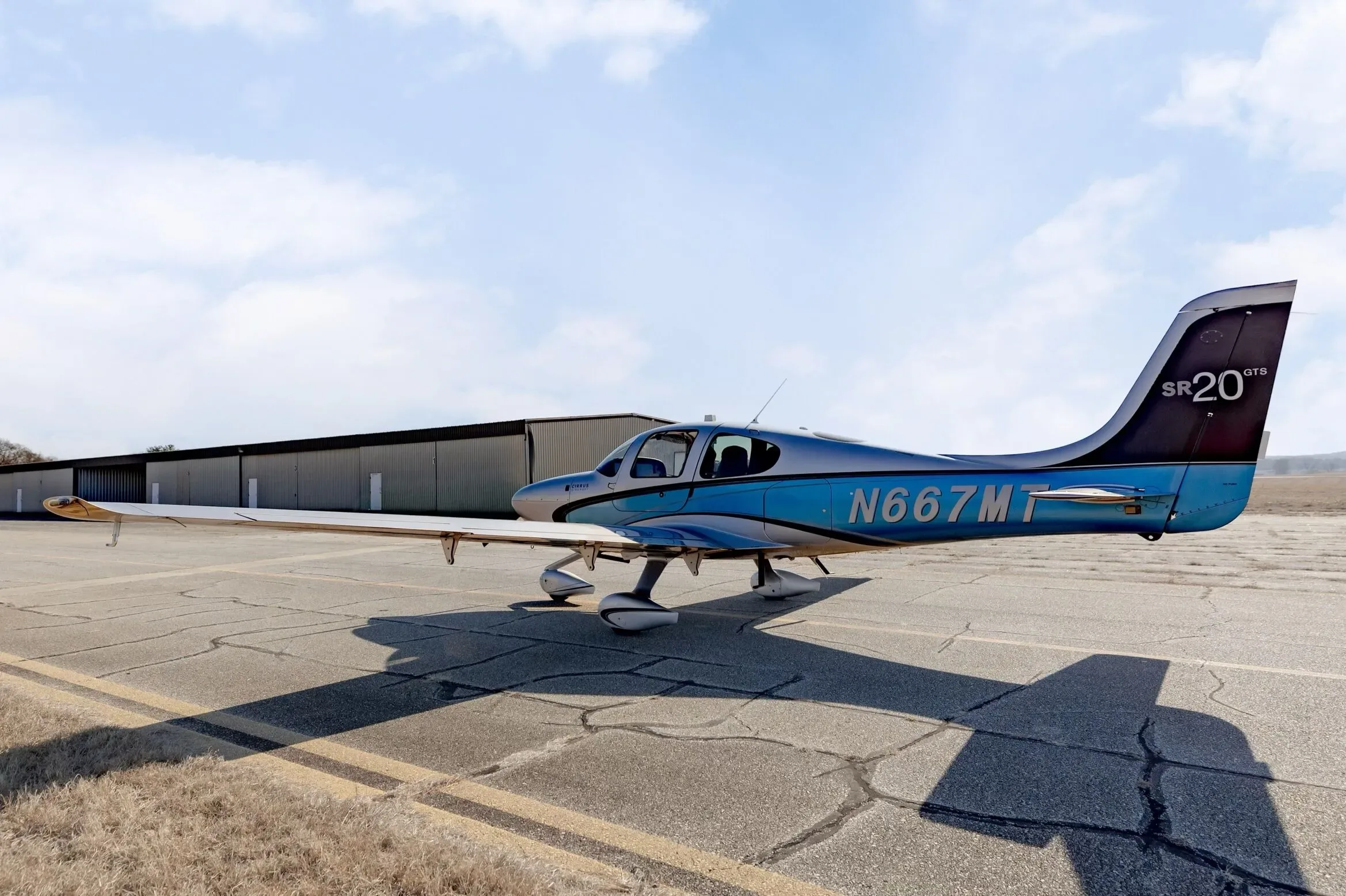 A Cirrus SR20 GTS aircraft with N667MT registration parked on an airfield next to a long hangar building.