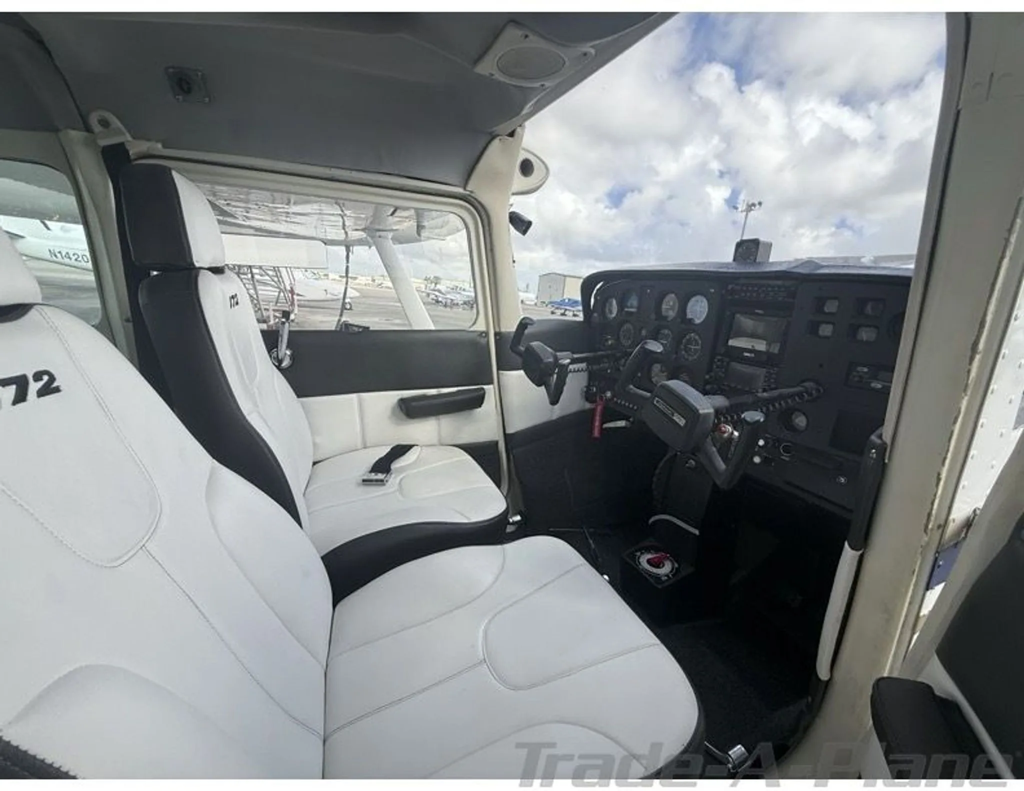 White and black interior of a Cessna 172 cabin, showing the front seats and part of the instrument panel.