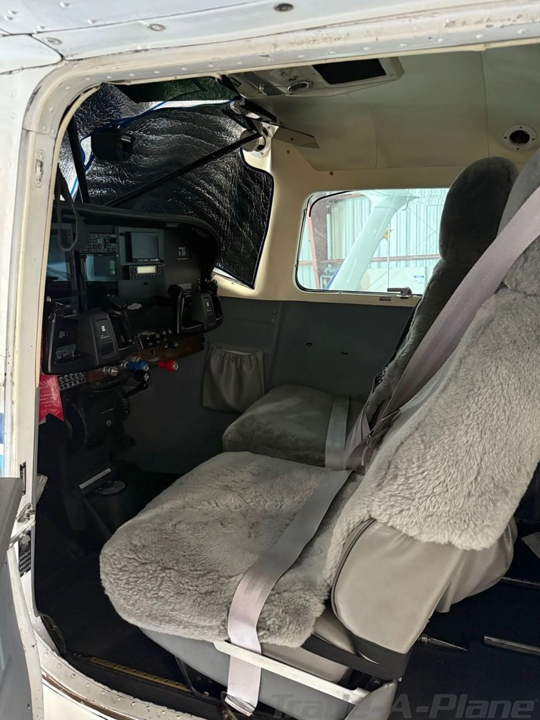 View of the front cabin seats with gray sheepskin covers and a partial view of the cockpit in the Cessna 206 Stationair.