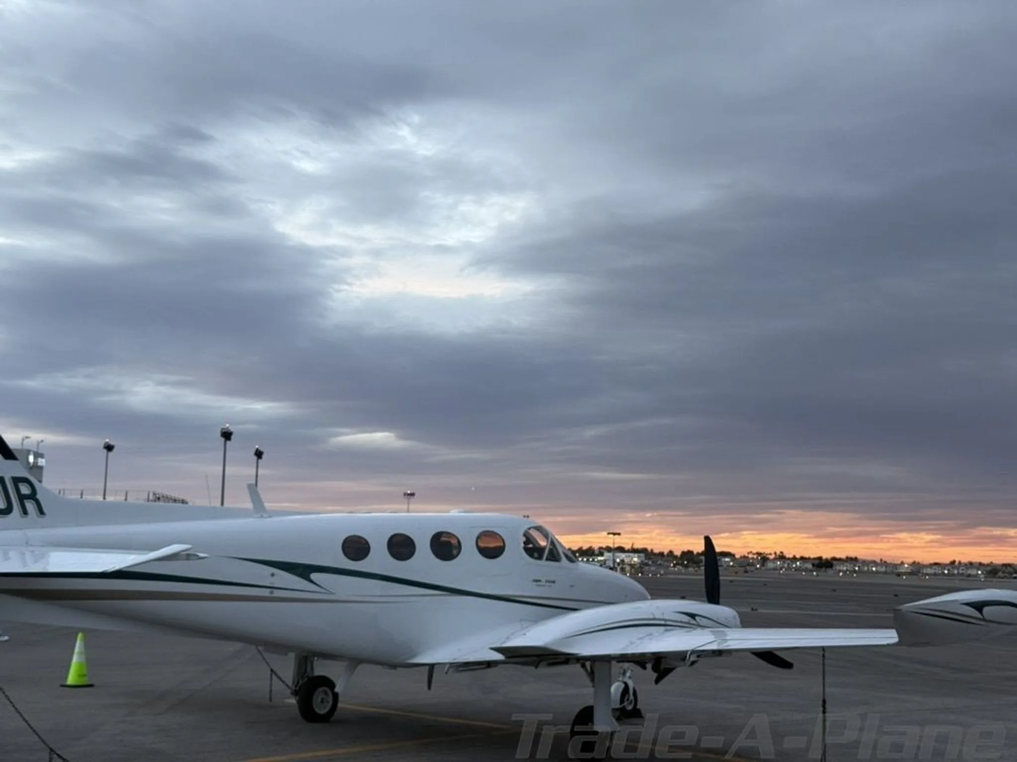 A white twin-engine aircraft, N653JR, is parked on a tarmac with a vibrant sunset sky in the background.