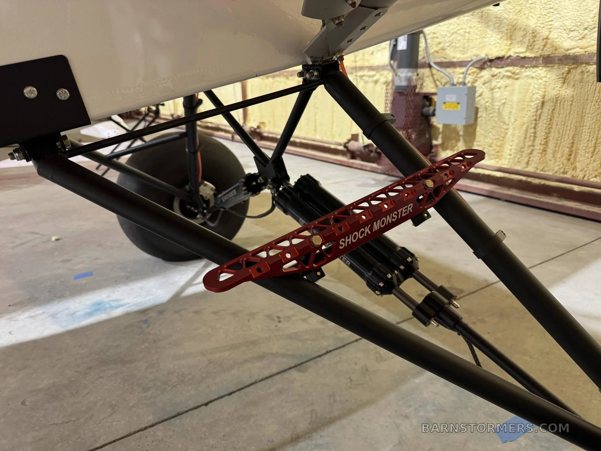 A close-up view of the black landing gear struts and red "SHOCK MONSTER" shock absorbers of a light aircraft.