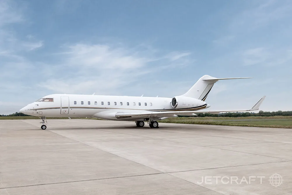 A white Bombardier Global business jet with gold and black stripes seen from the side on an airfield.