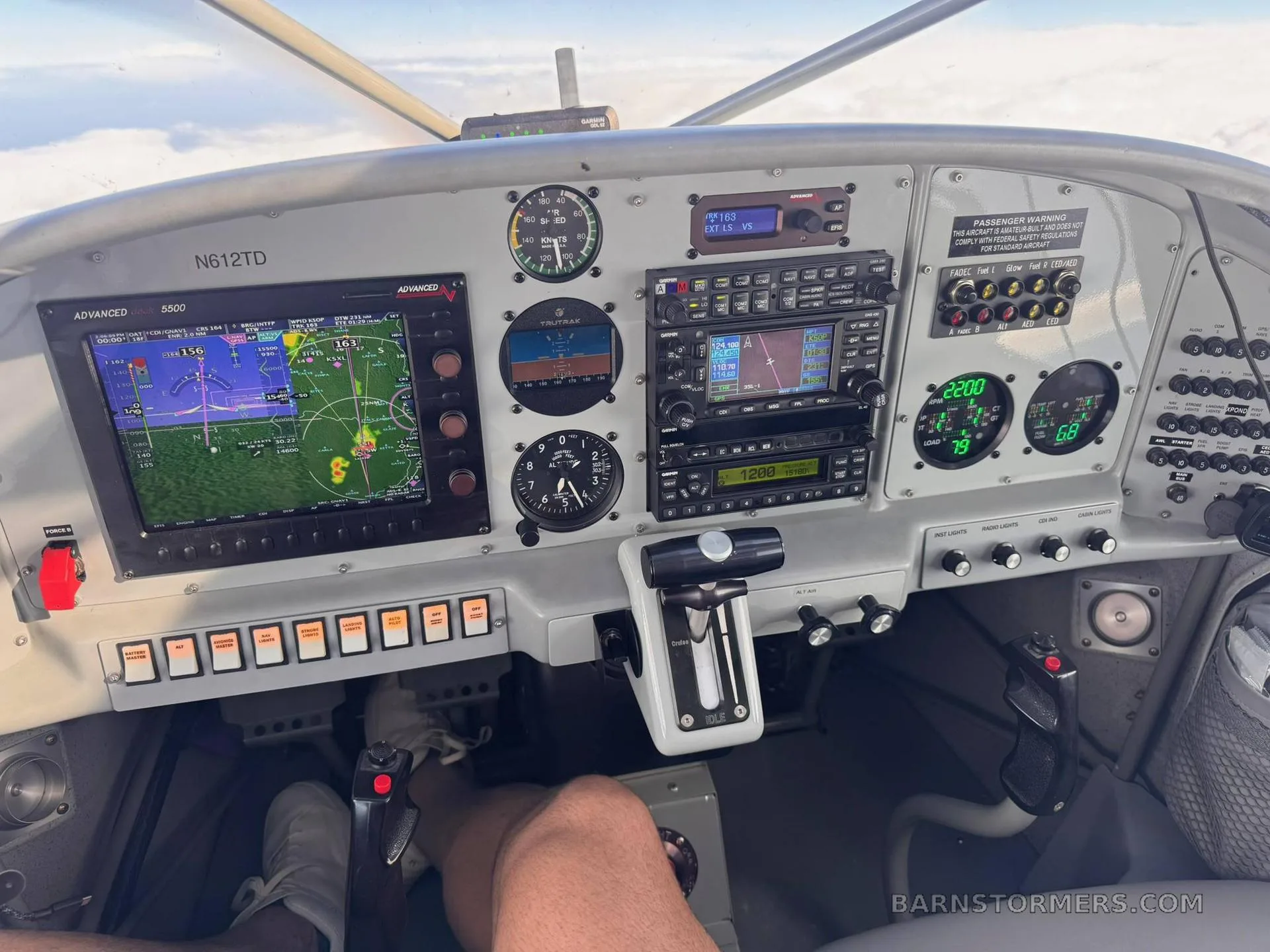The cockpit of a small aircraft showing a detailed instrument panel with multiple screens and gauges, with a pilot's legs visible.