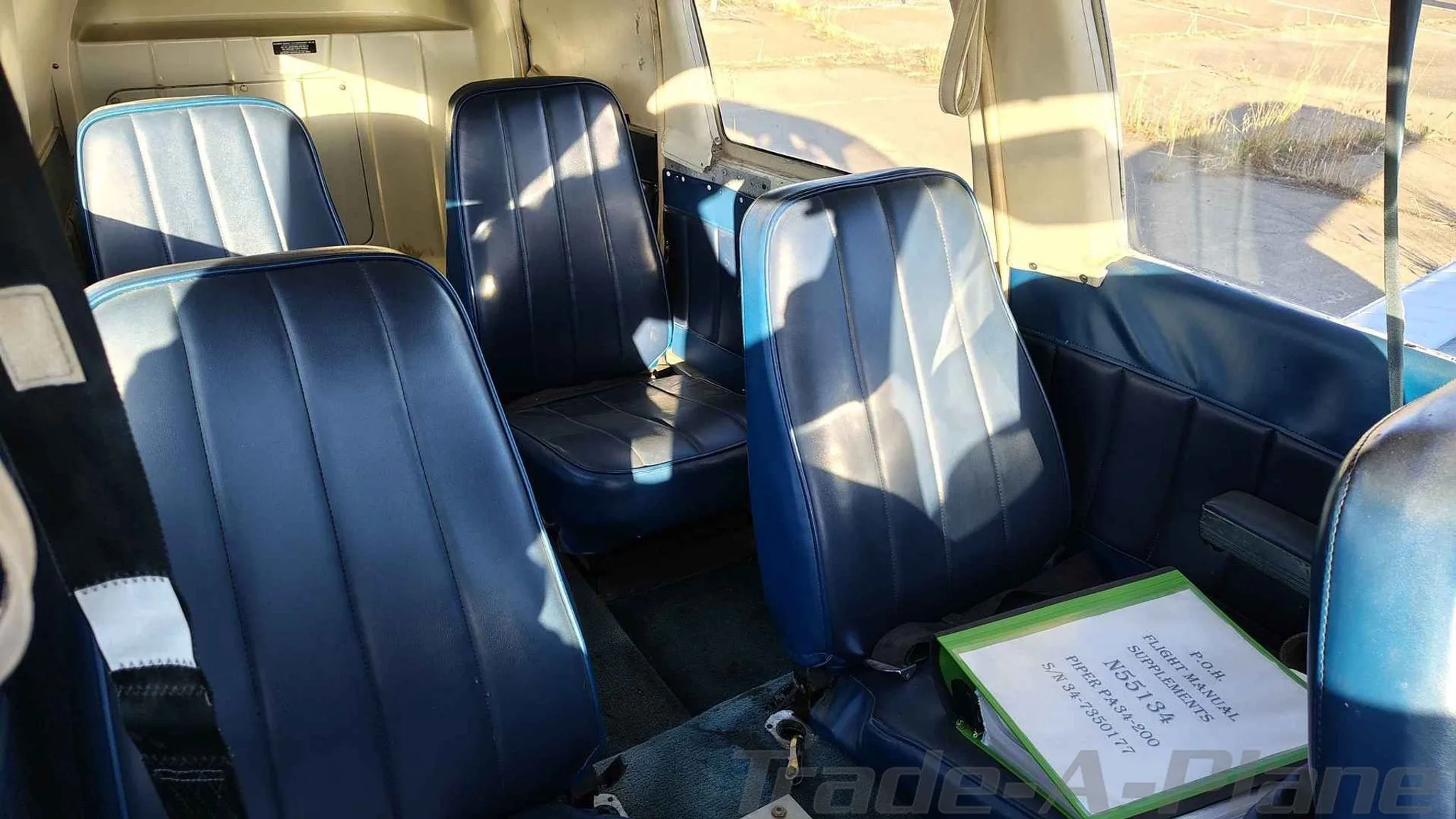 The blue rear cabin seats of a Piper PA-23-200, with a flight manual showing N55134.