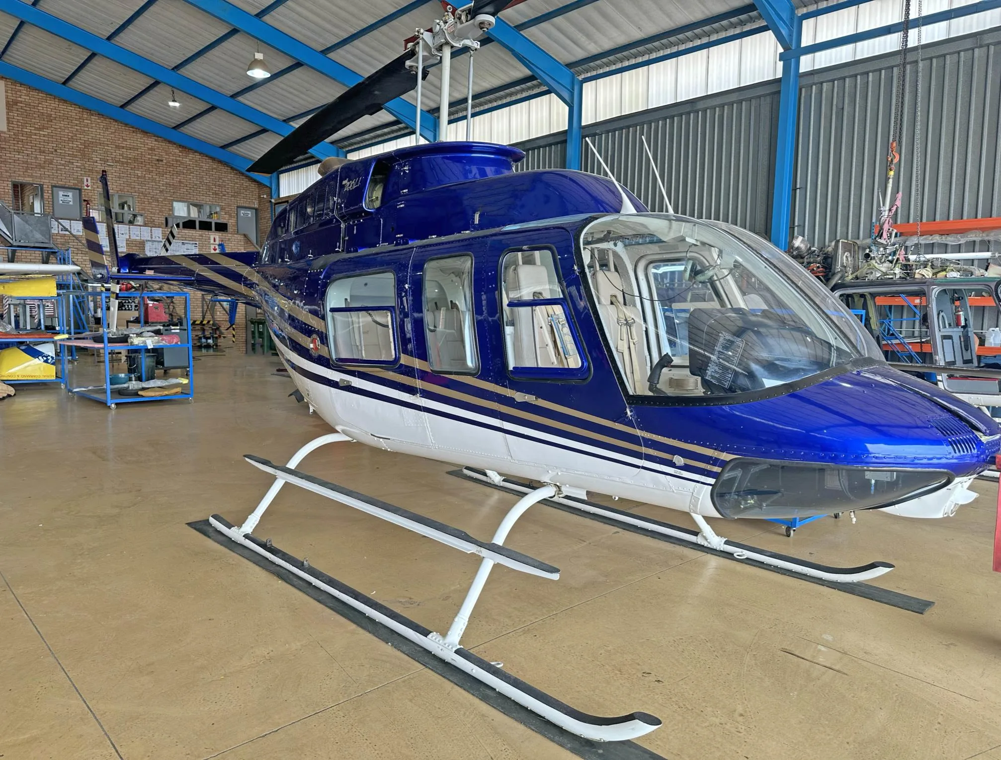 A blue and white Bell 206L-4 LongRanger helicopter with gold stripes parked inside a hangar.