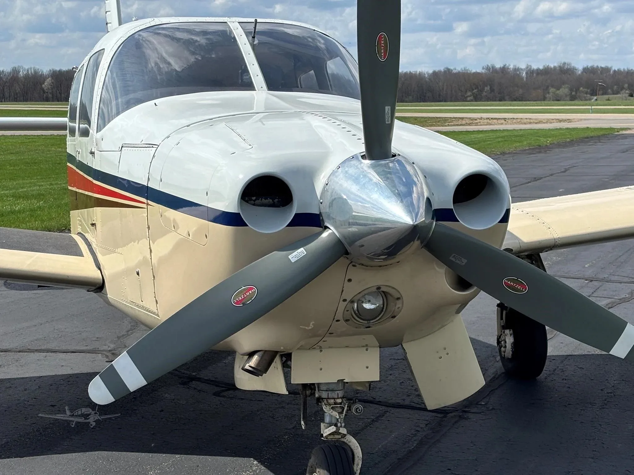 A close-up front view of the propeller and nose of a white and beige single-engine aircraft.