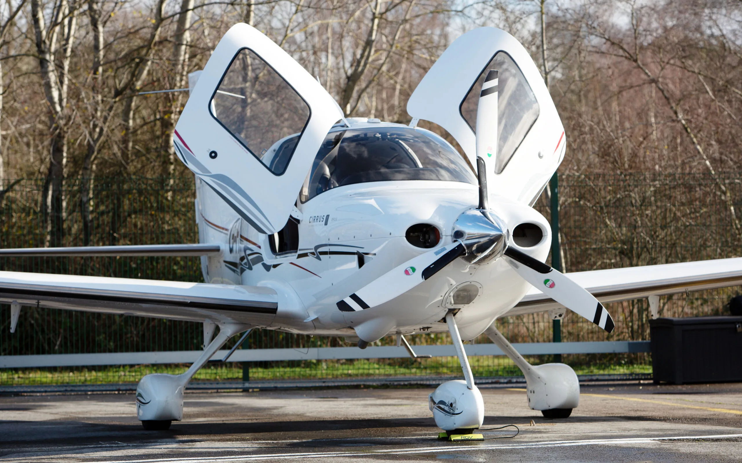 A white Cirrus SR22 G3 aircraft with red and black stripes, registration G-FELC, parked on a tarmac with its gull-wing doors open, viewed from the front.