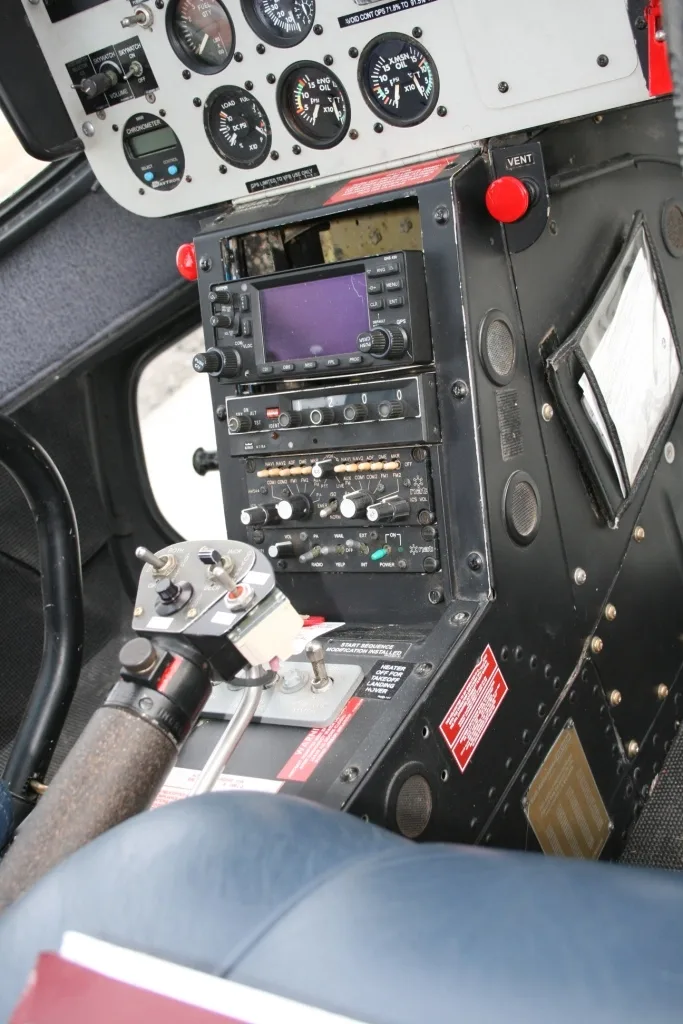 Close-up view of the lower instrument panel and cyclic/collective controls in a helicopter cockpit.