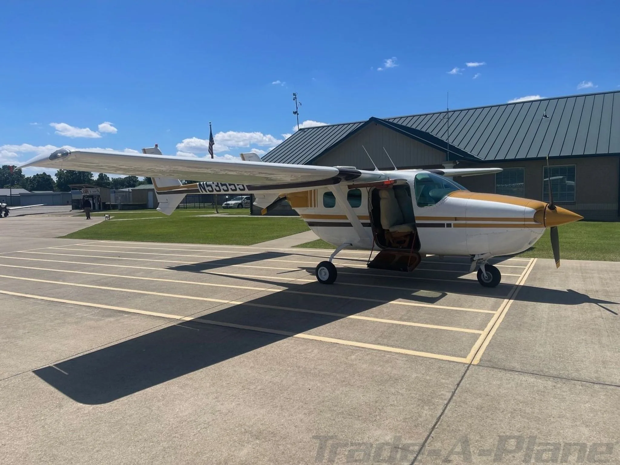 A white and gold Cessna 206 aircraft with its door open, parked on an airfield tarmac.