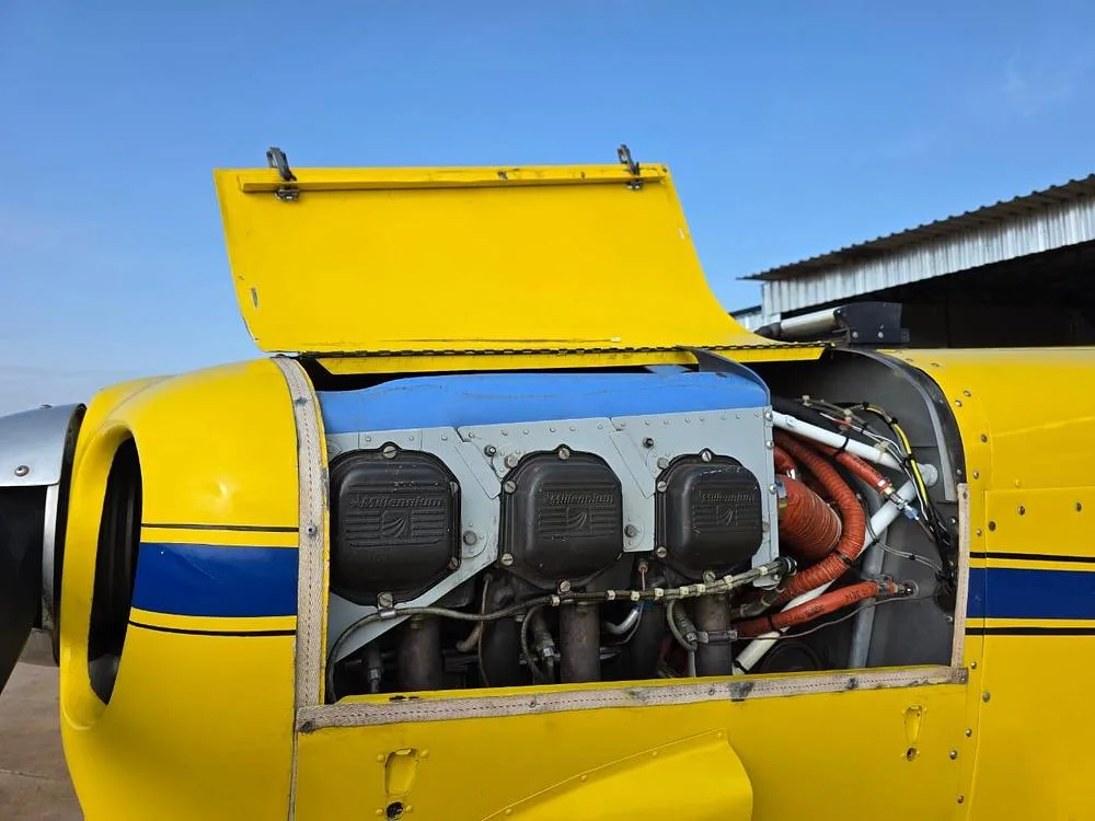 A close-up of the yellow aircraft's engine compartment with the cowling open, revealing the engine cylinders.