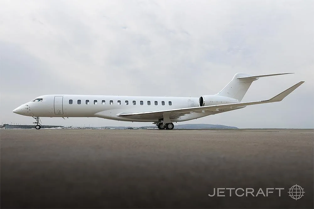 A white Bombardier Global 7500 business jet is parked on an airport tarmac under a cloudy sky.