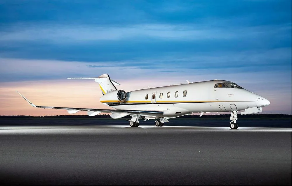 A white N157PH business jet with yellow and grey stripes is parked on an airfield at dusk.