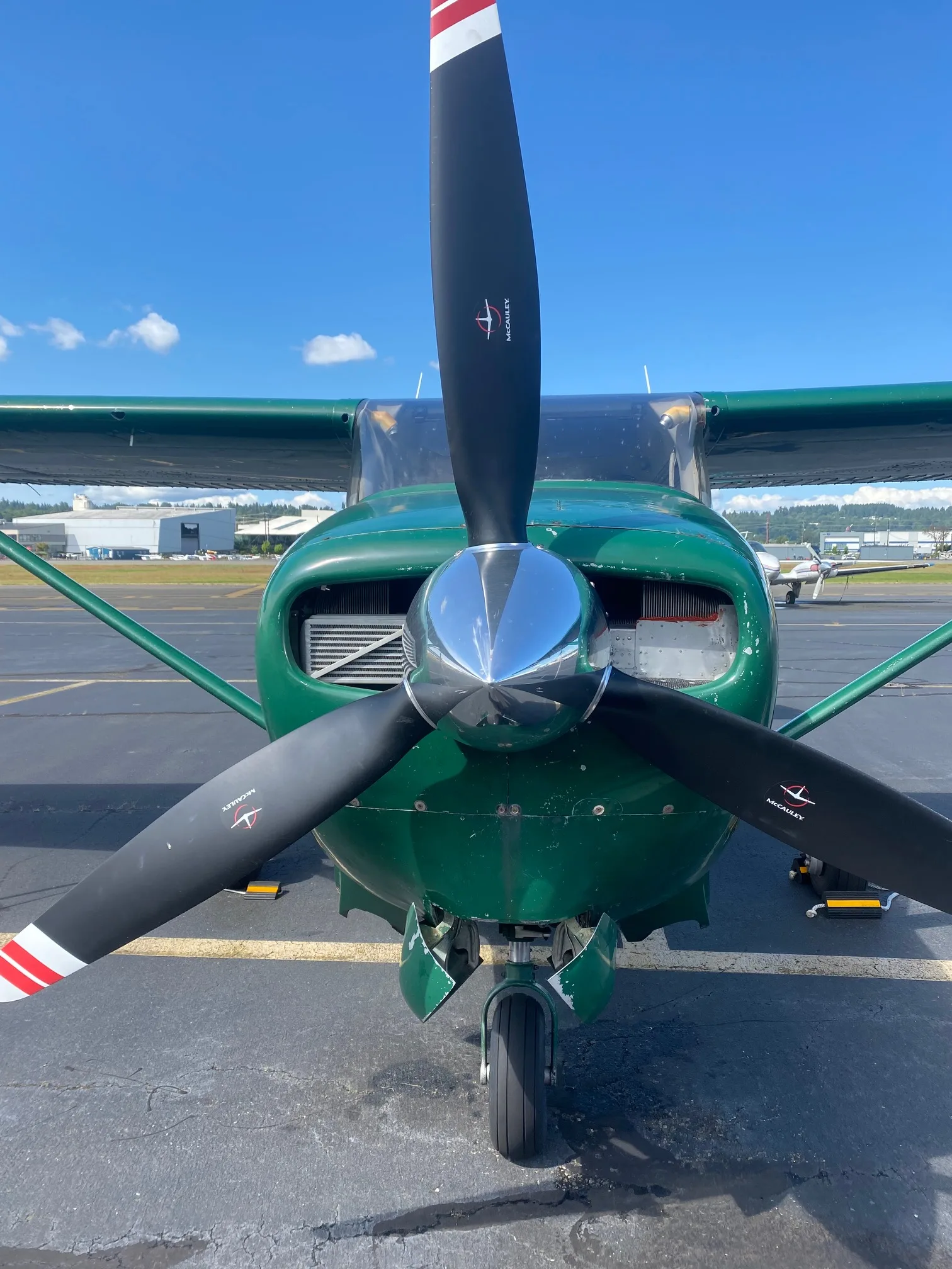 Front view of a green Cessna 210 aircraft with a three-bladed propeller on an airfield.
