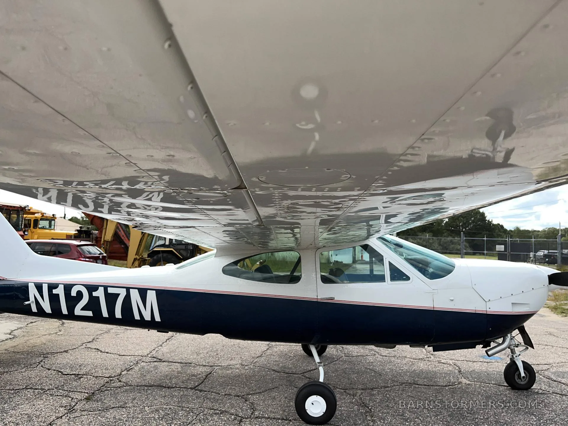 Side view of the white and dark blue single-engine propeller aircraft N1217M, showing the underside of the wing and fuselage.
