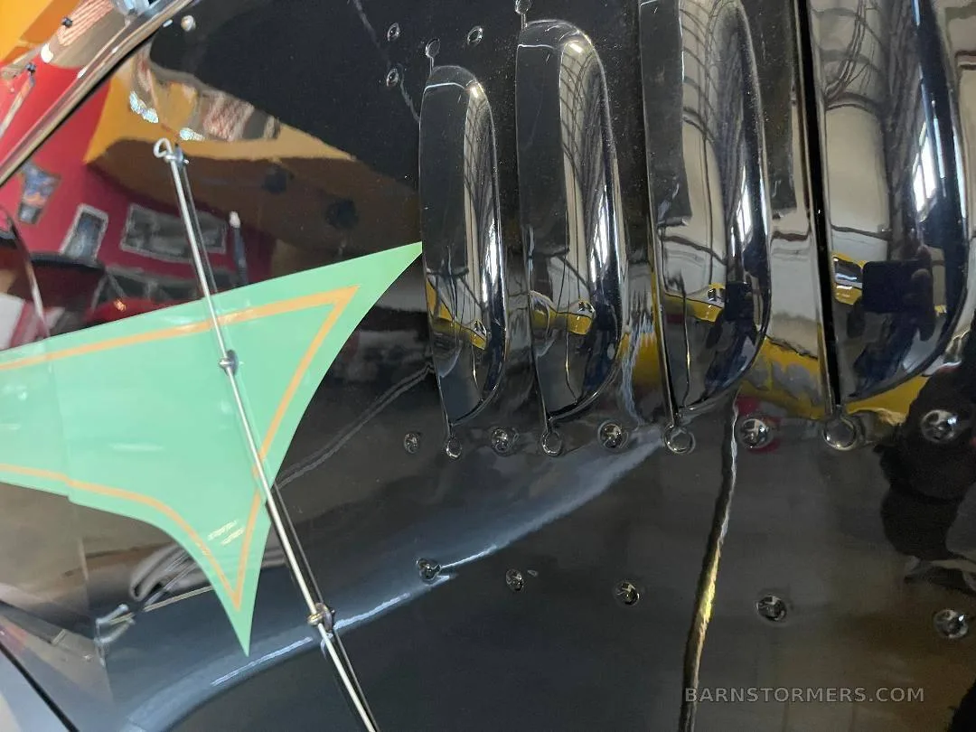 A close-up view of the black fuselage of a biplane shows engine vents and a green and orange paint detail.