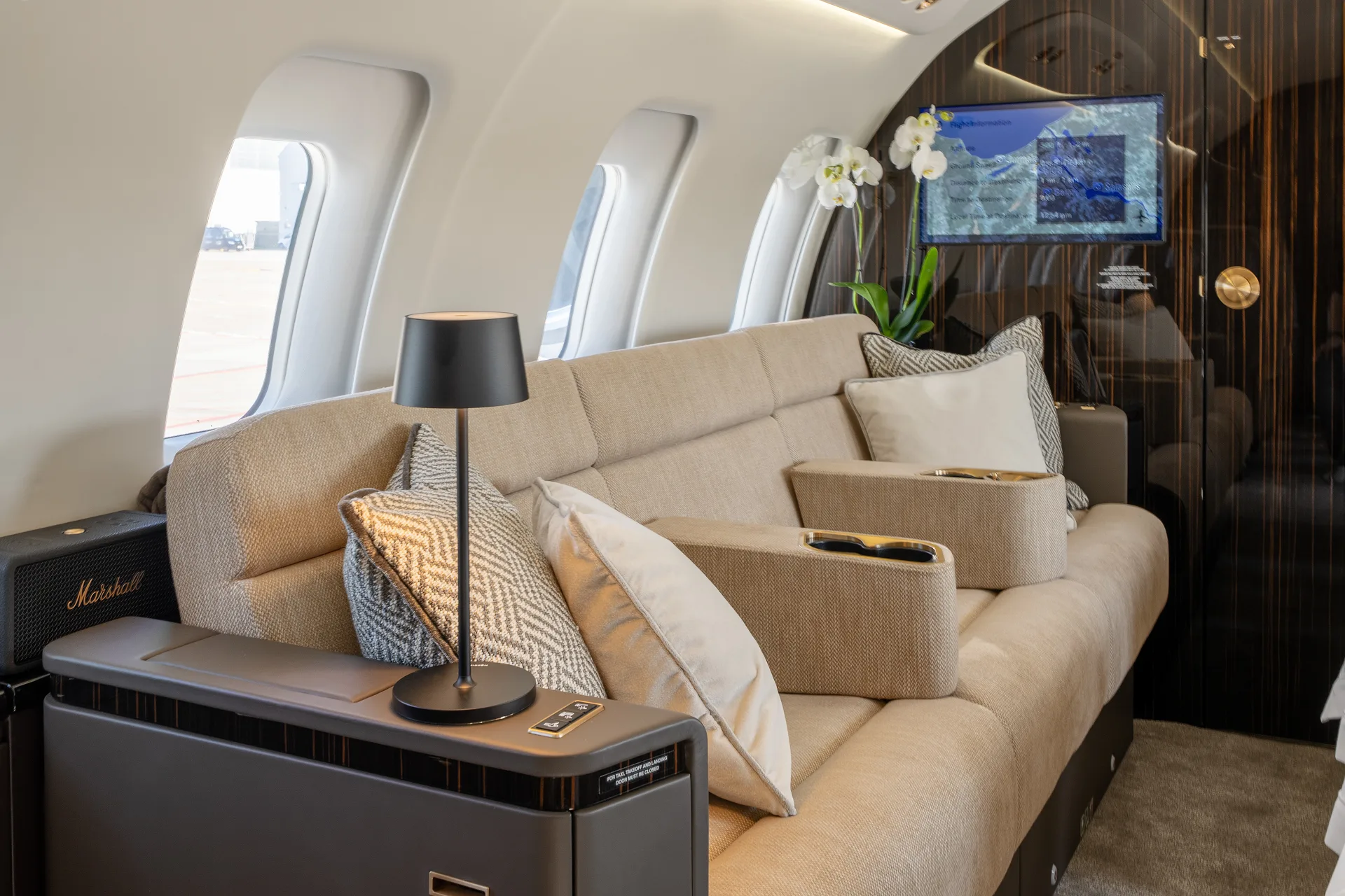 A comfortable beige sofa with pillows and a side table with a lamp inside the aircraft cabin.