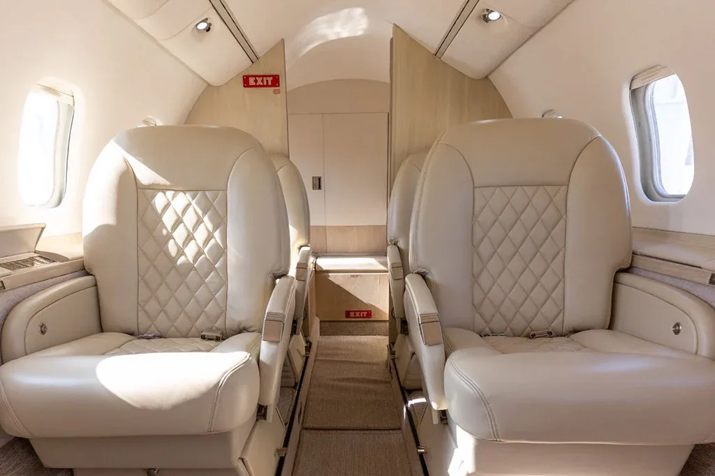 The luxurious cabin interior of a Learjet, featuring beige quilted leather seats and an aisle view towards the rear.