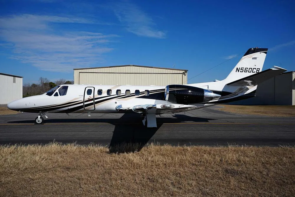 A white Cessna Citation Encore business jet with black and gold stripes, tail number N560CB, parked on an airfield.