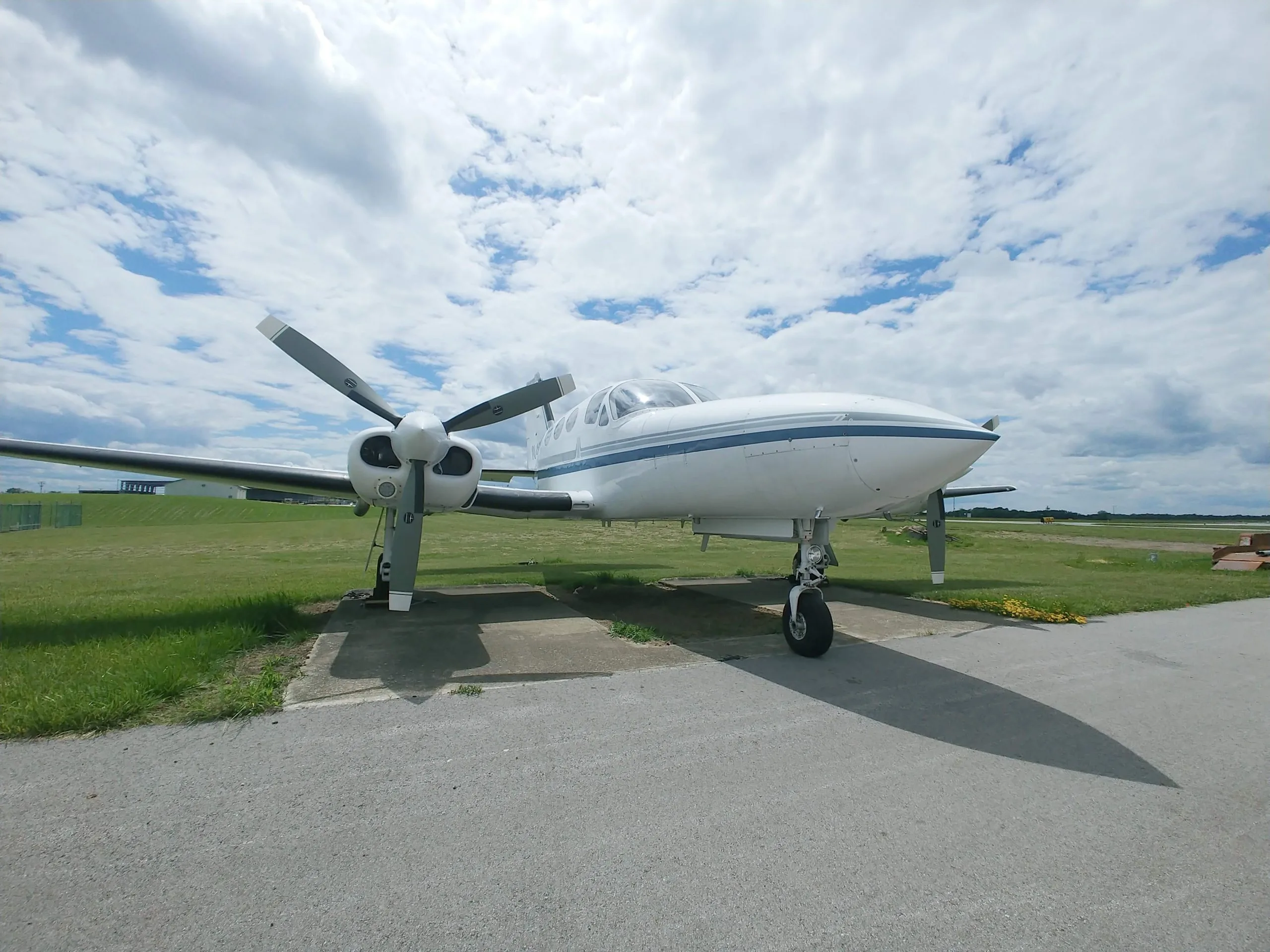 A white and blue twin-engine aircraft is parked on the tarmac under a cloudy sky.