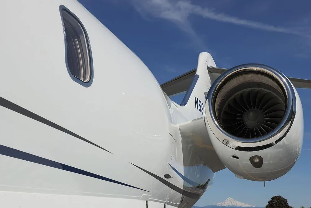 A close-up view of the rear fuselage and engine of a white business jet, showing the registration N59, with a snow-capped mountain in the distance.